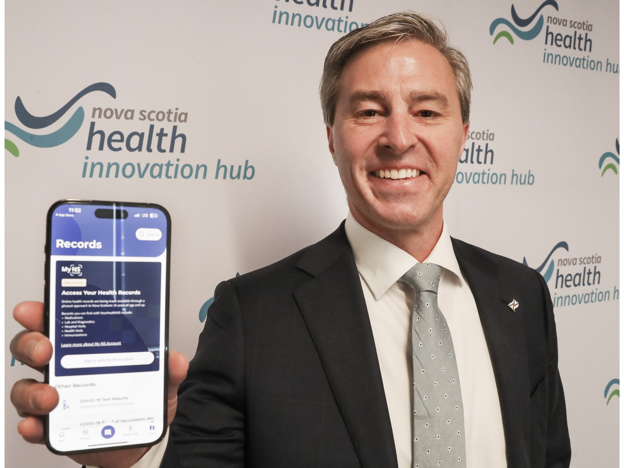 Photo of Premier Tim Houston holding up a smartphone open to the YourHealthNS app