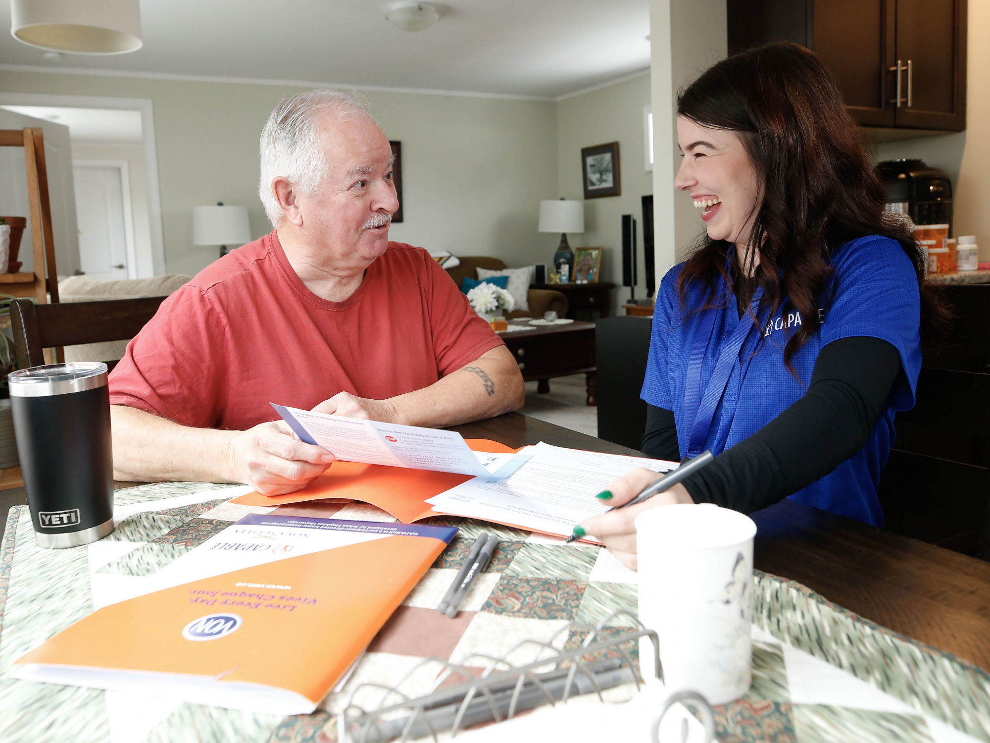 Photo of a senior citizen and occupational therapist talking at a table with papers on it 