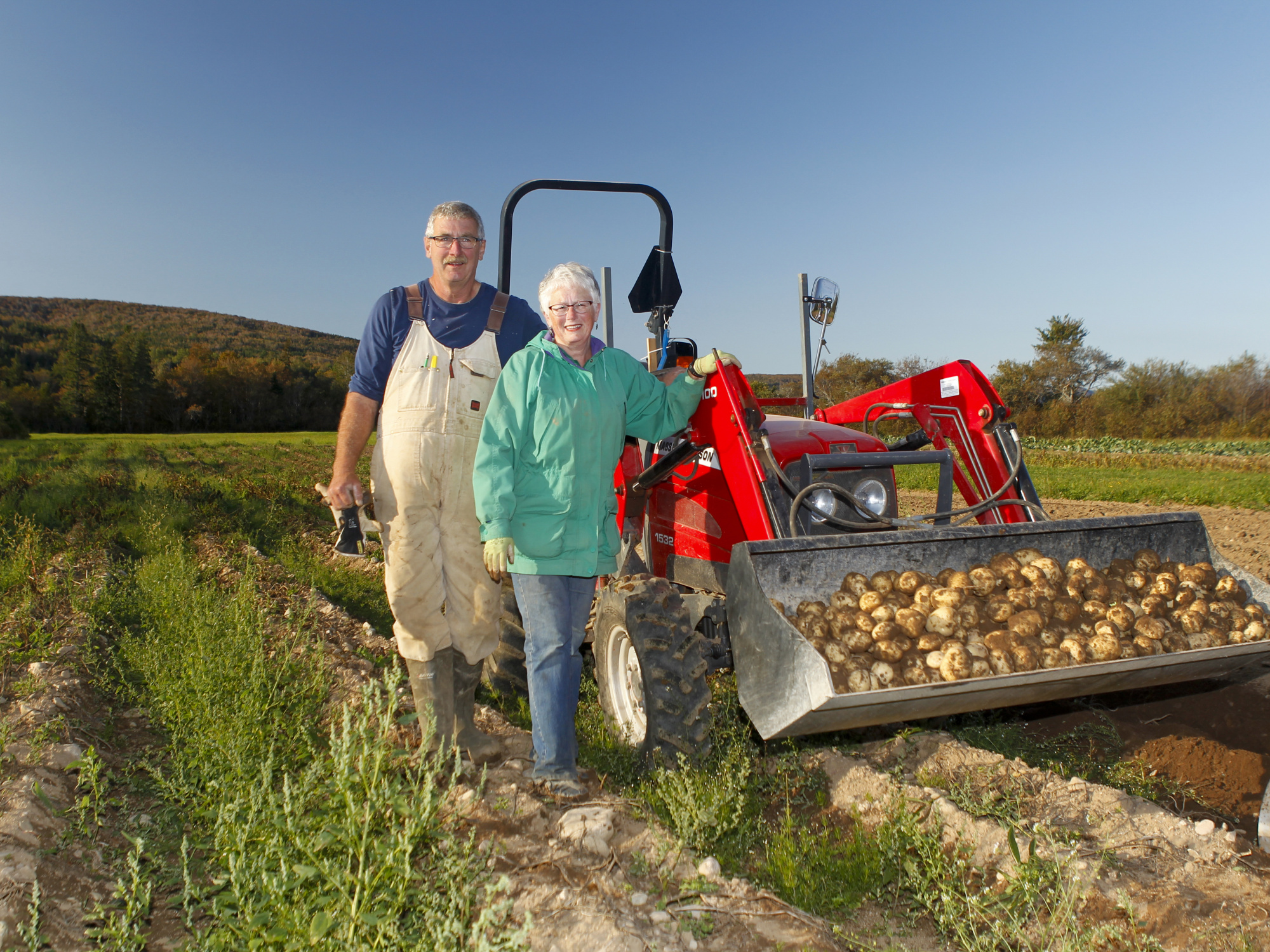 Photo of two farmers standing beside a tractor in a field.