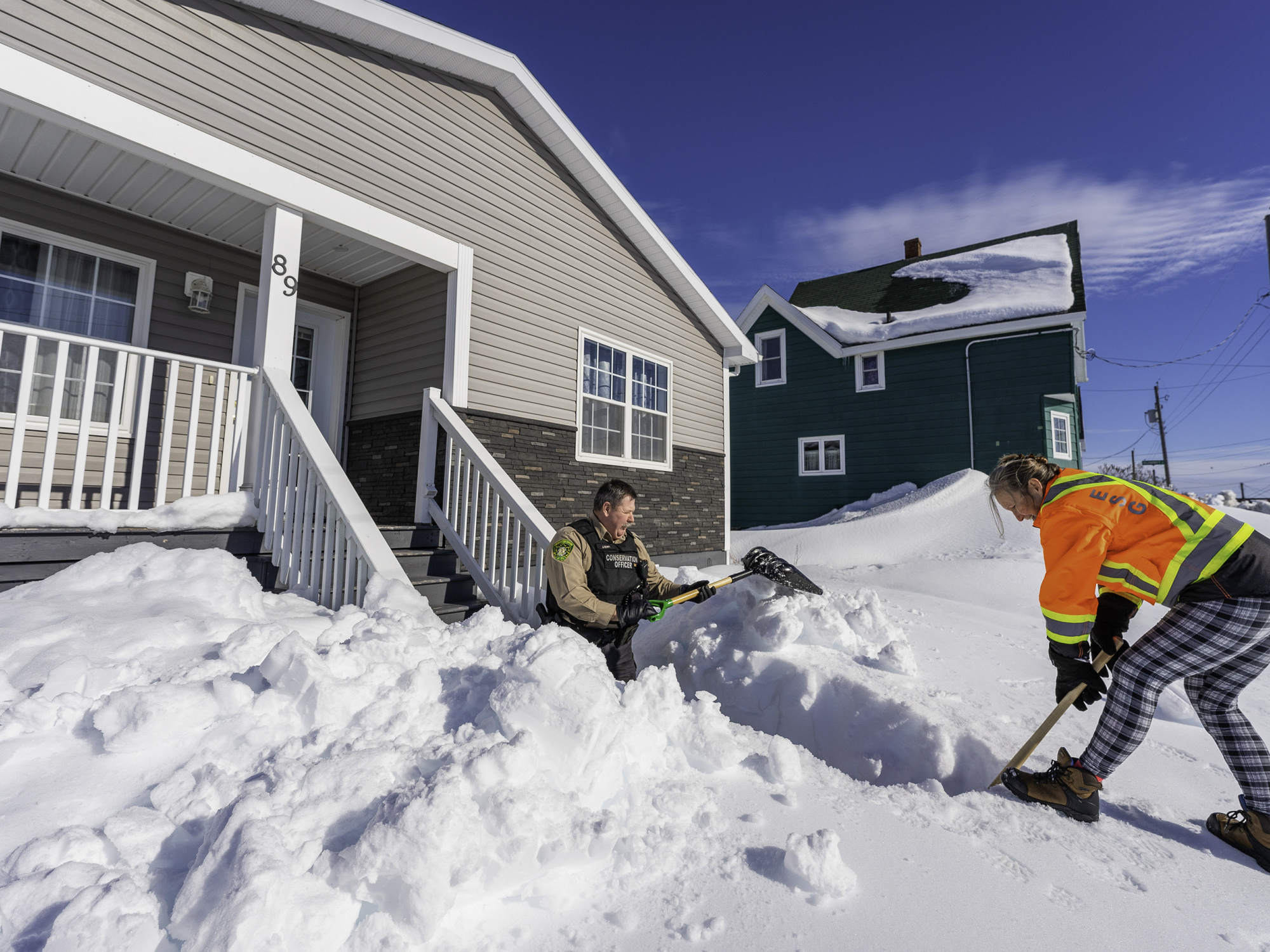 Department of Natural Resources and Renewables staff shovel out the entryway to a home.