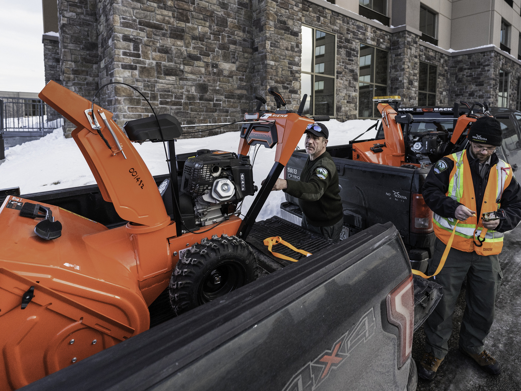 Department of Natural Resources and Renewables staff load snowblowers into the back of pickup trucks.