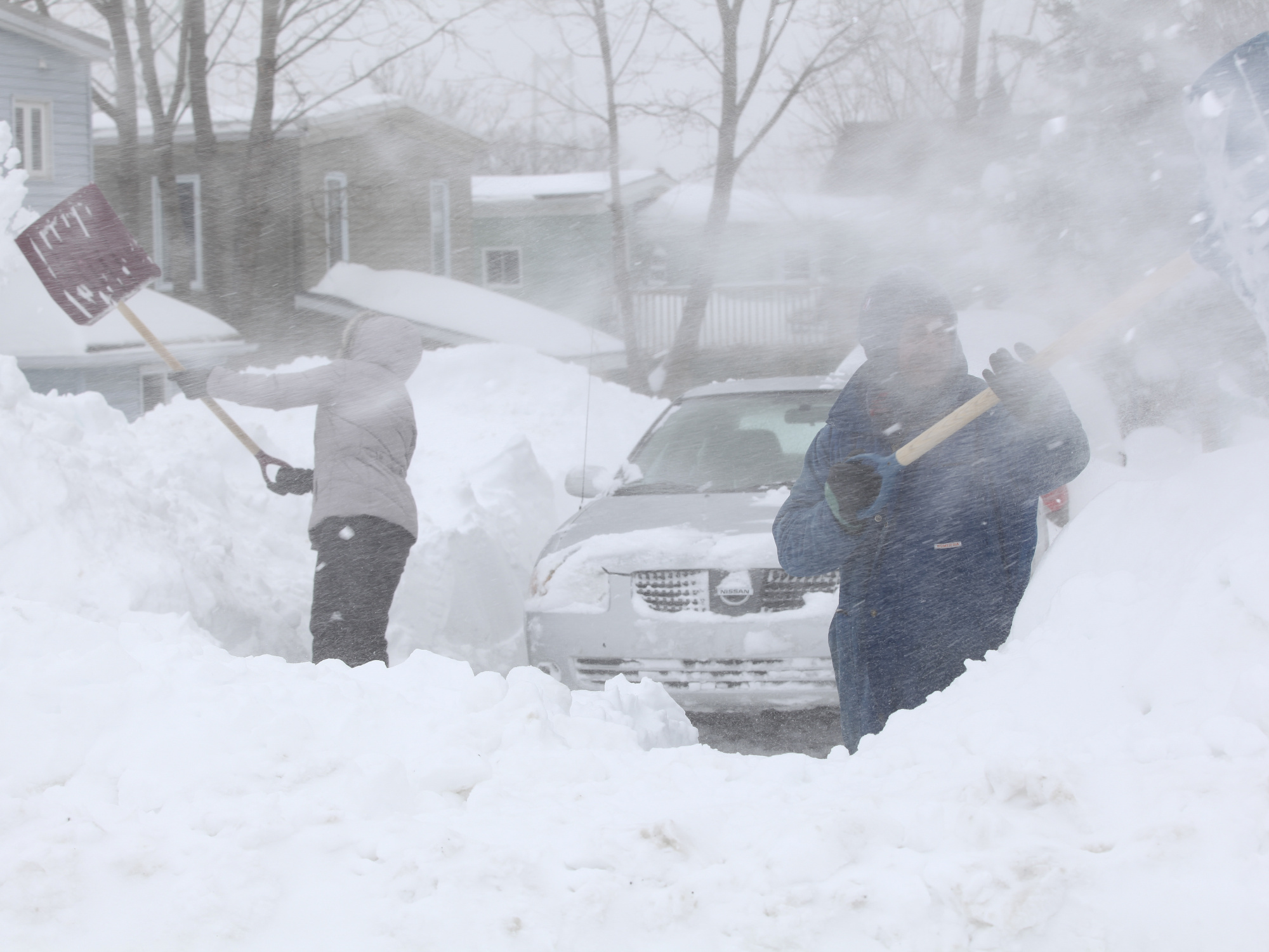 photo of two people shovelling a driveway as the snow blows around them