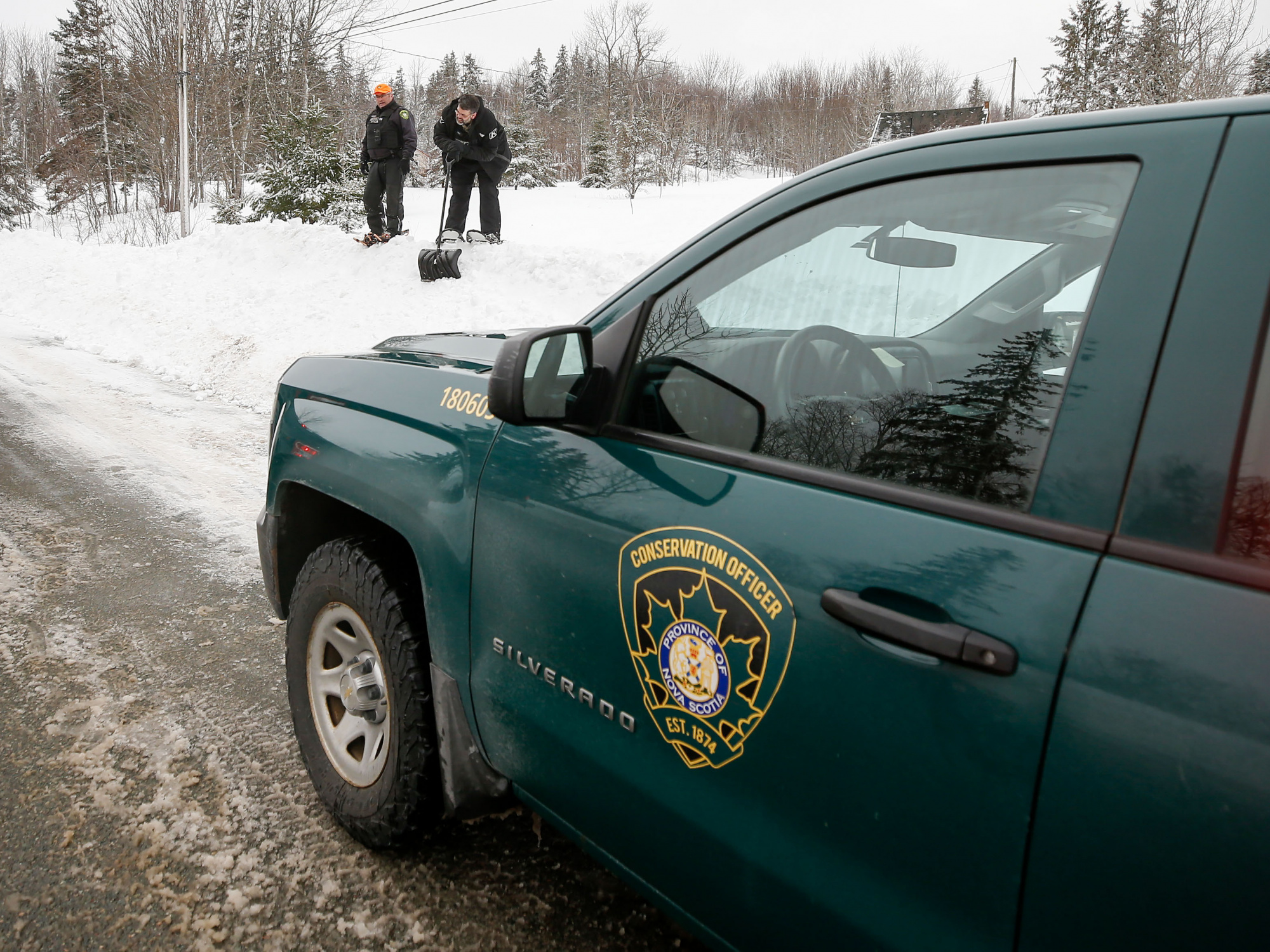 Photo of conservation officers' truck in the foreground and two officers on a snowbank