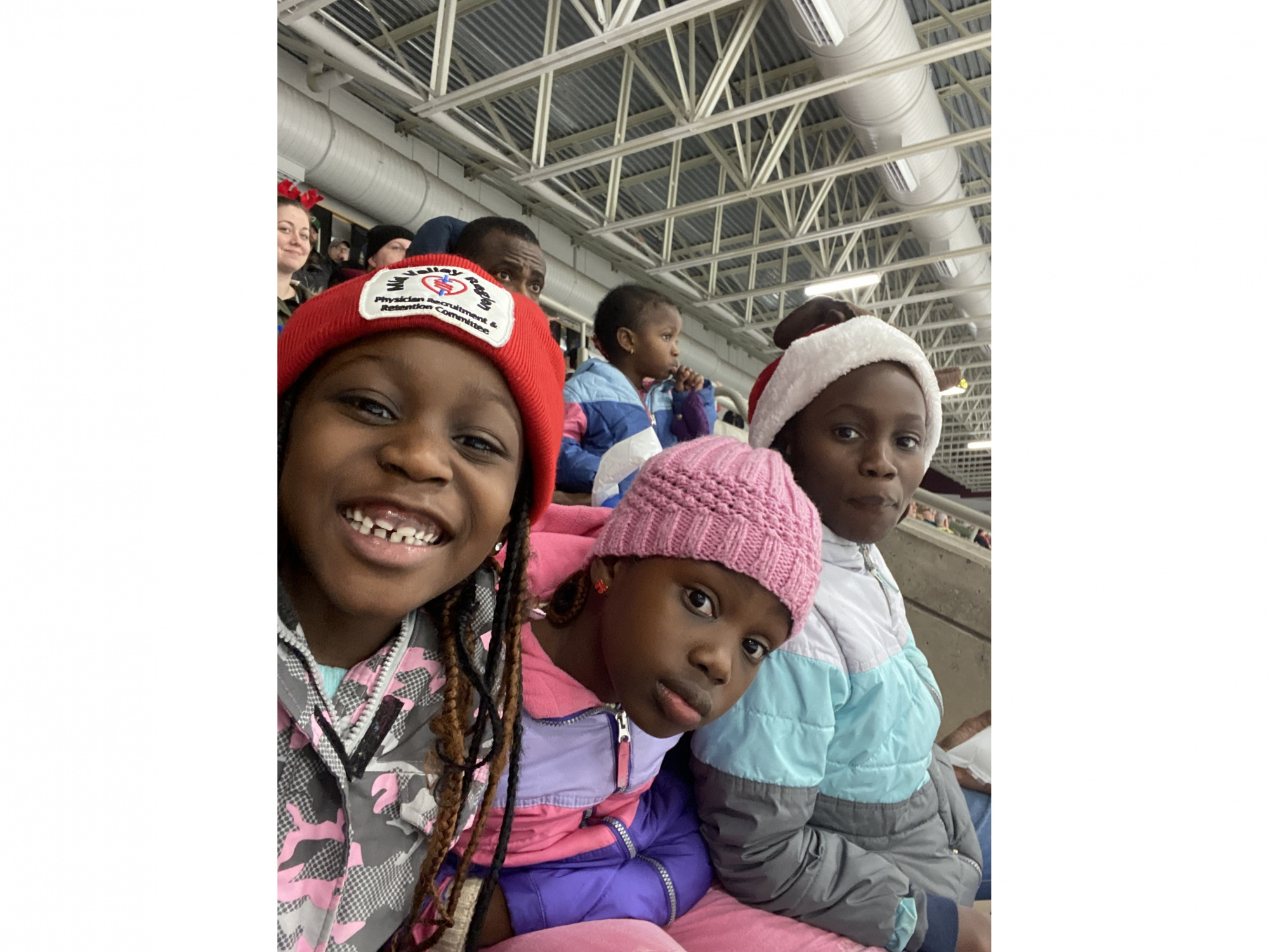 Three children sitting together in the bleachers at a hockey game
