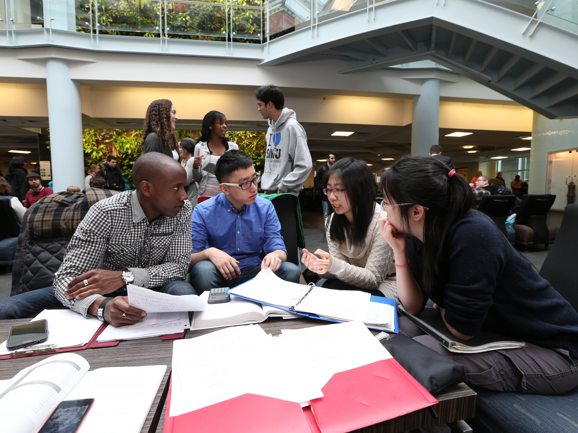Photo of four students engaged in conversation around a table containing papers and folders