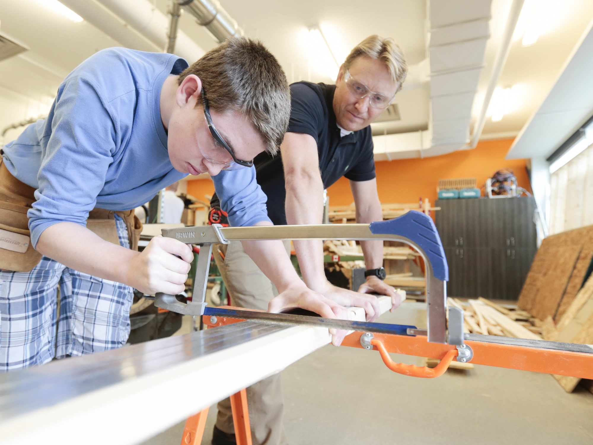 Photo of a student using a hacksaw watched by an instructor