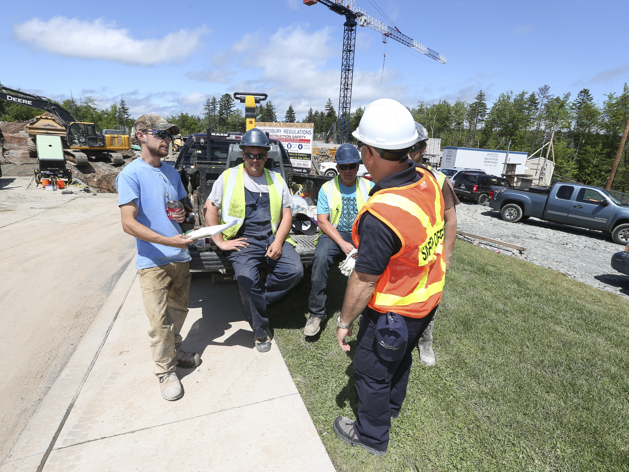 Construction workers chat at a job site with heavy equipment in the background. 