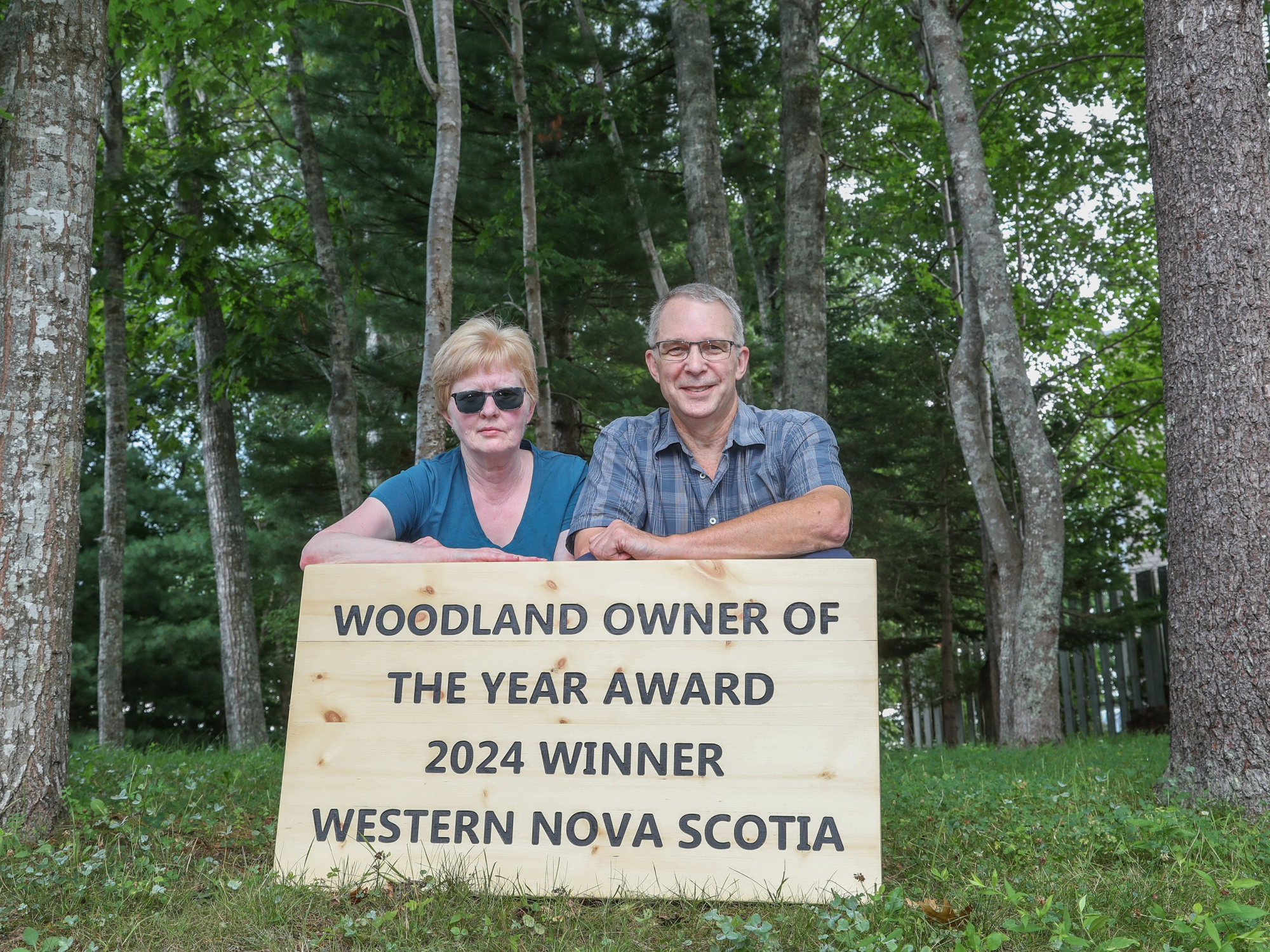 Photo of a woman and man in the woods with a sign that says Woodland Owner of the Year Award 2024 Winner Western Nova Scotia