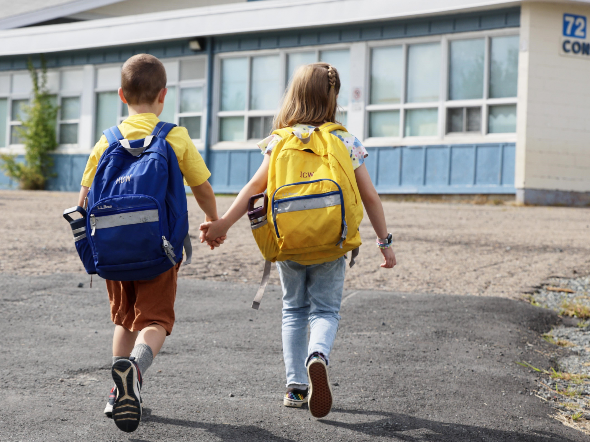 Photo of two young children with backpacks holding hands walking to school