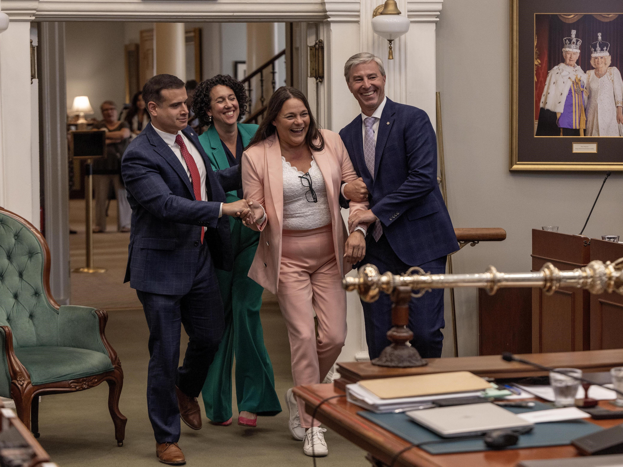 Photo of Premier Tim Houston, Official Opposition Leader Zach Churchill and NDP Leader Claudia Chender escorting new House Speaker Danielle Barkhouse in the legislative chamber