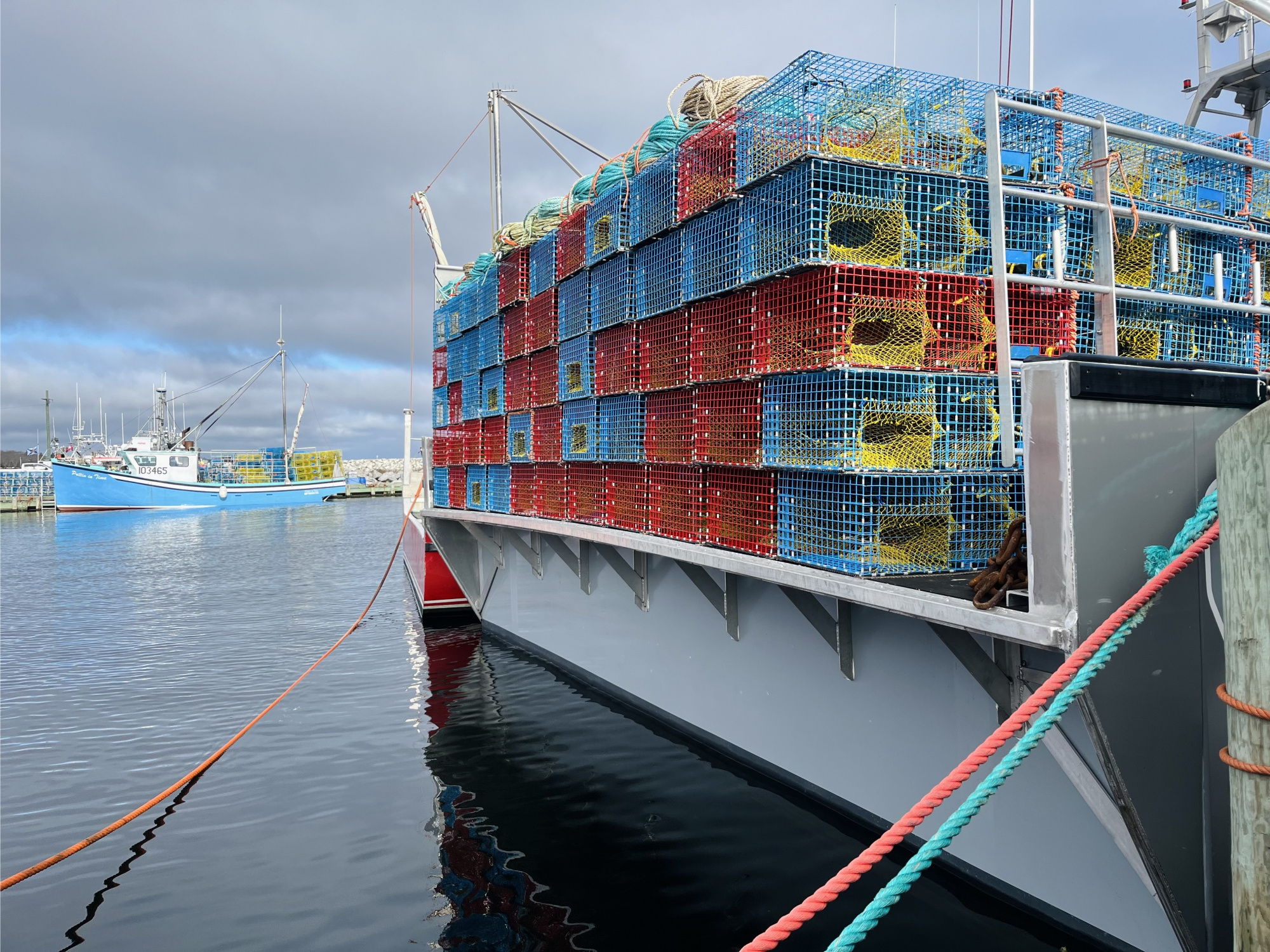 A docked boat holding many lobster traps, with a second boat and traps in the background