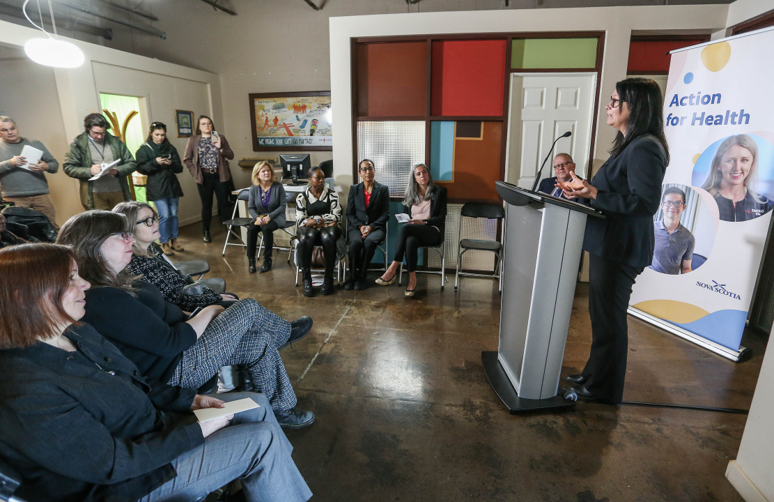 A photo showing Health and Wellness Minister Michelle Thompson at a podium speaking to people gathered to hear the announcement