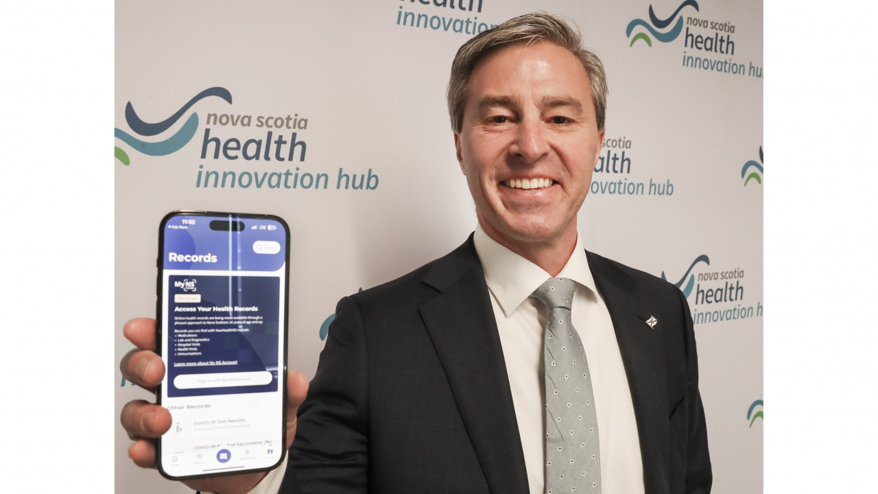Photo of Premier Tim Houston holding up a smartphone open to the YourHealthNS app