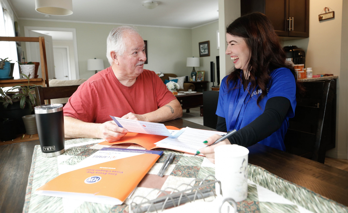 Photo of a senior citizen and occupational therapist talking at a table with papers on it 