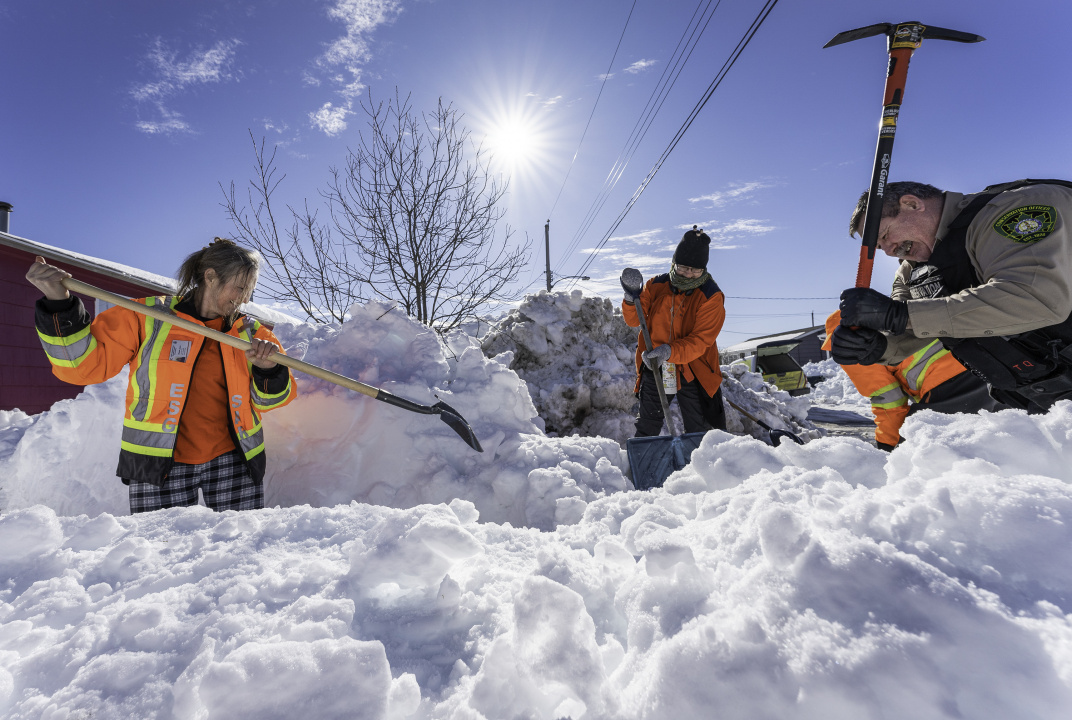 Staff work with tools to clear snow from a driveway.