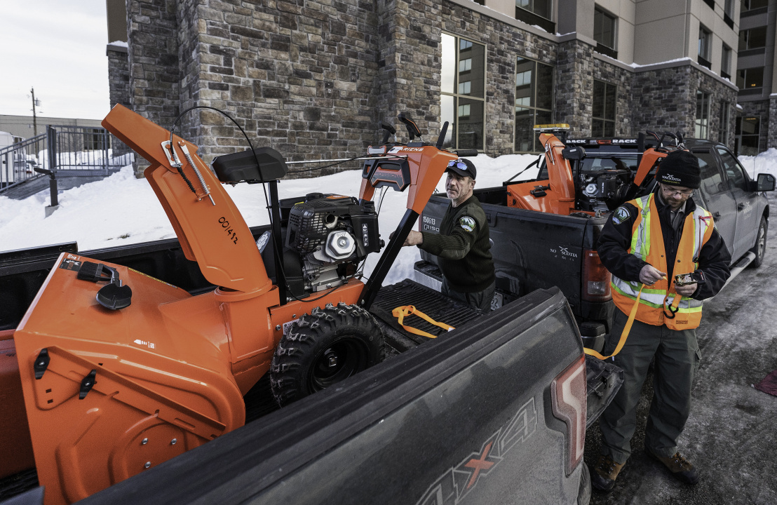 Department of Natural Resources and Renewables staff load snowblowers into the back of pickup trucks.