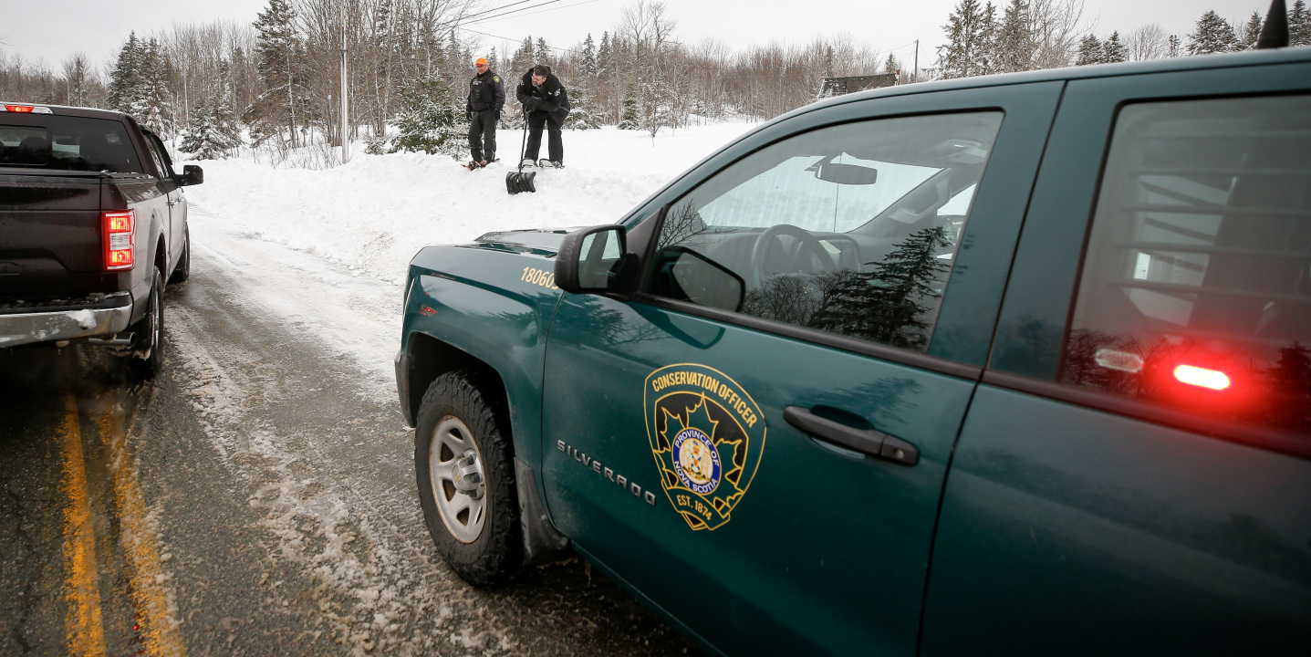 Photo of conservation officers' truck in the foreground and two officers on a snowbank