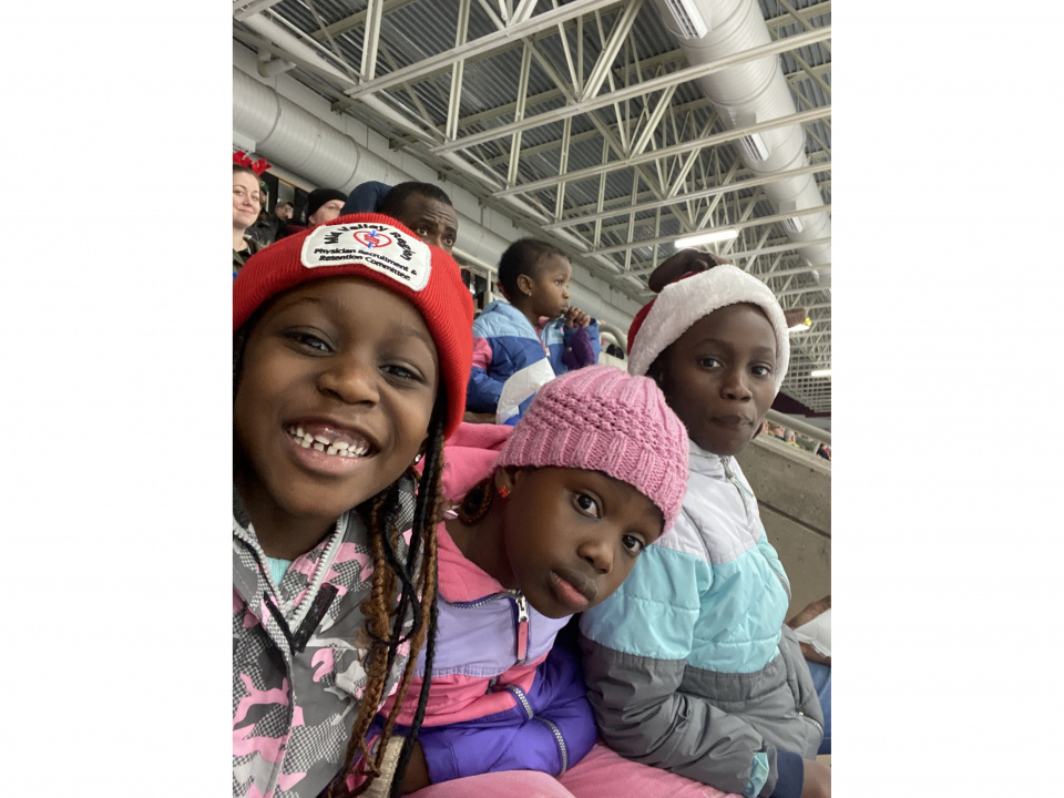 Three children sitting together in the bleachers at a hockey game