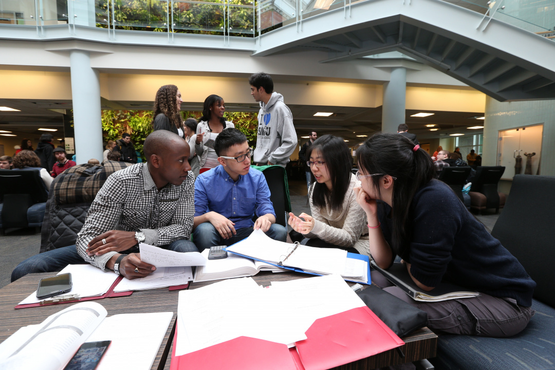 Photo of four students engaged in conversation around a table containing papers and folders