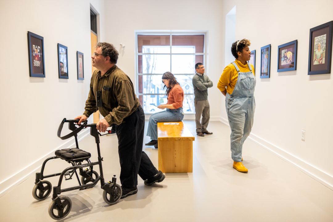 Photo of people, including a person using a walker, looking at art in a gallery setting