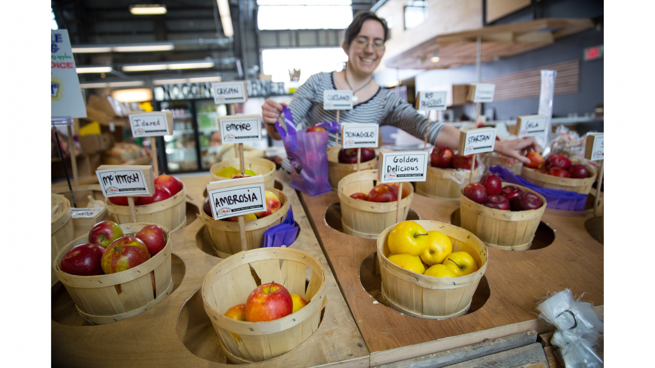 Photo of vendor and baskets of apples at a farmers' market