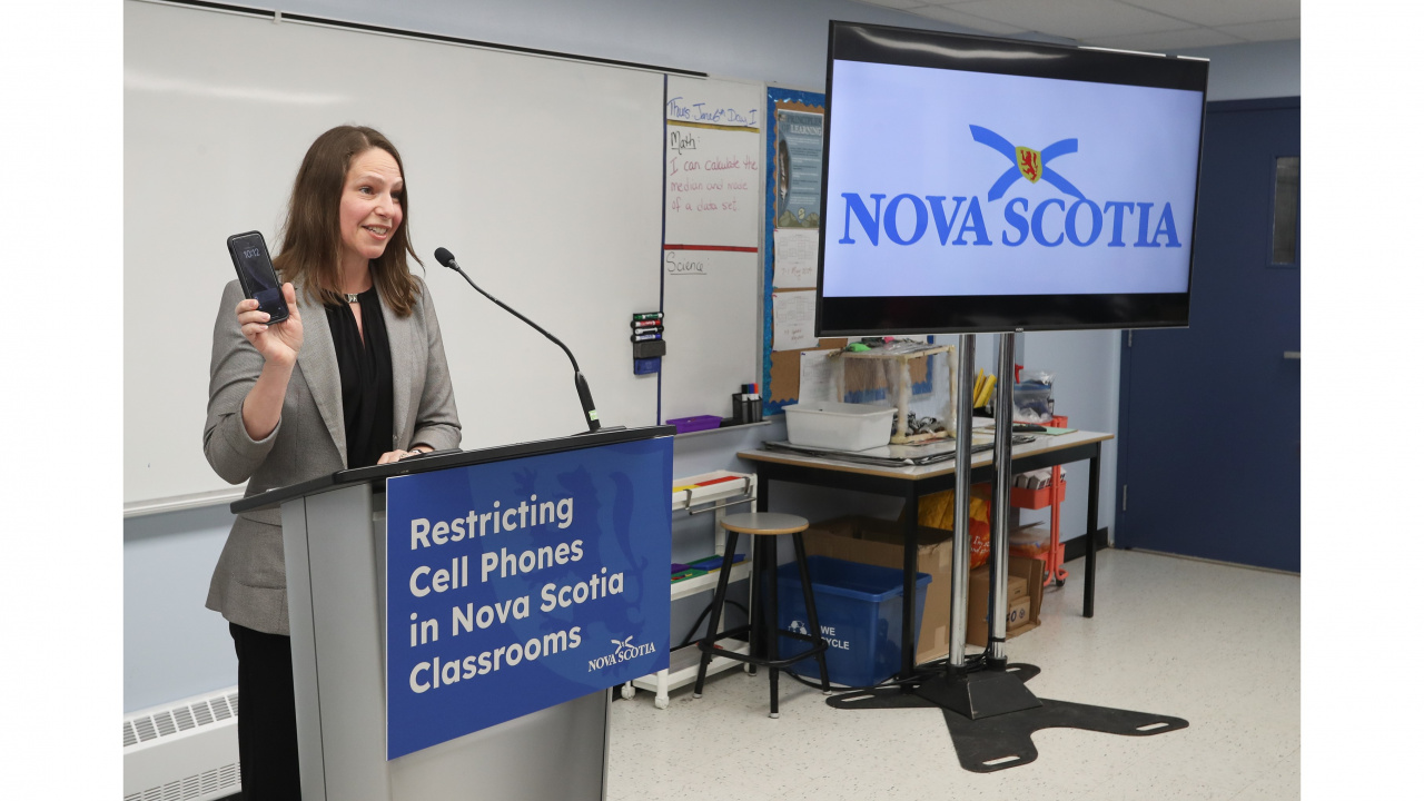 Photo of Education and Early Childhood Development Minister Becky Druhan holding up a cell phone at a podium