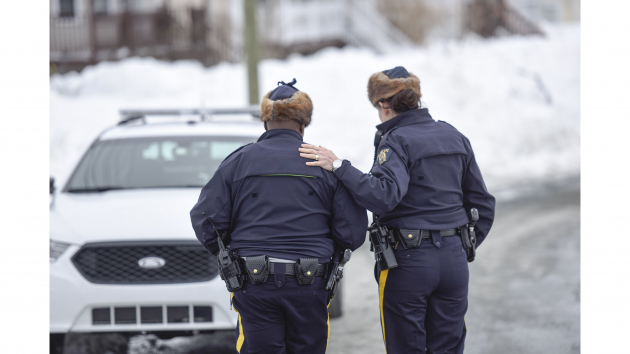 Photo from behind of RCMP officers walking toward cruiser and one officer's hand on the other's shoulder