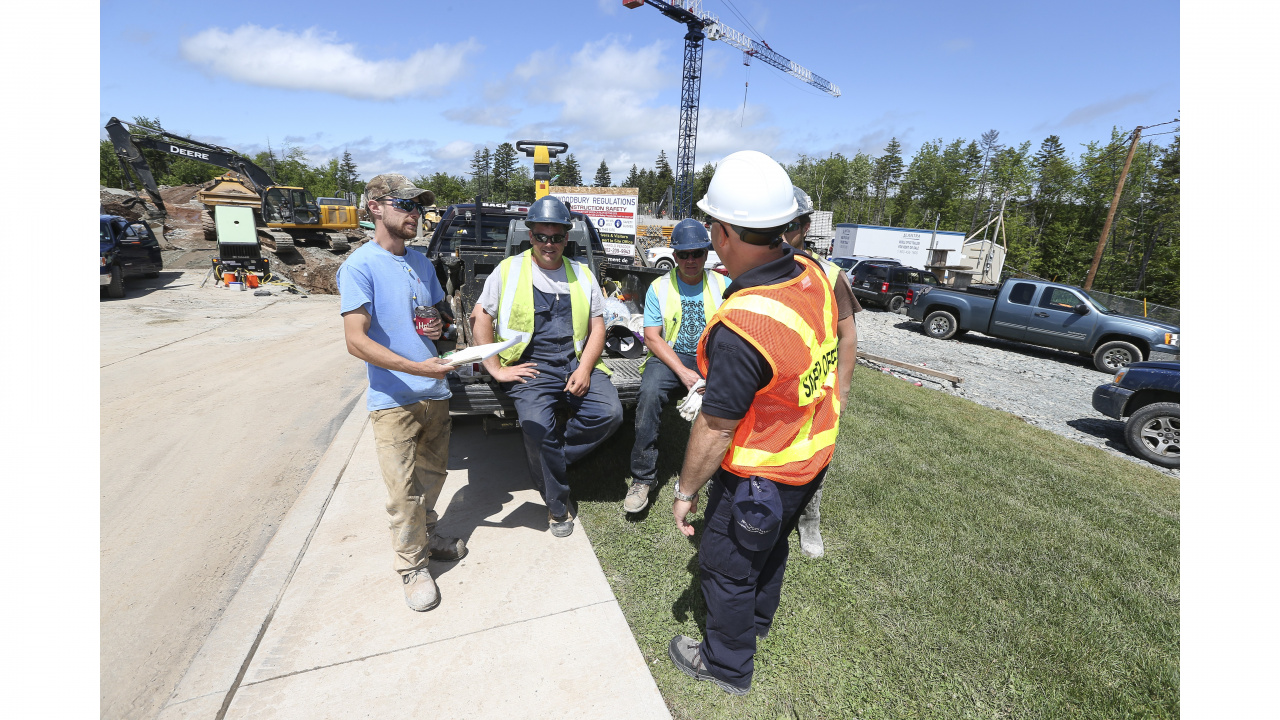 Construction workers chat at a job site with heavy equipment in the background. 