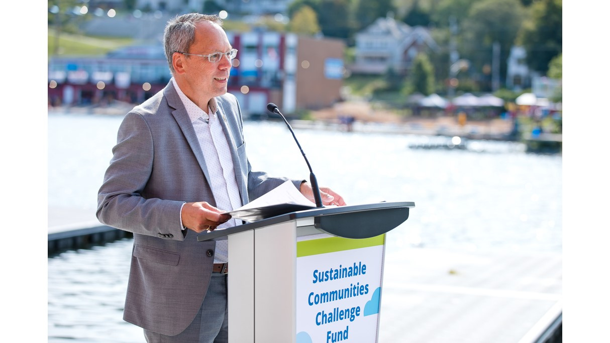 Minister Wong speaks from a podium with Lake Banook in the background.