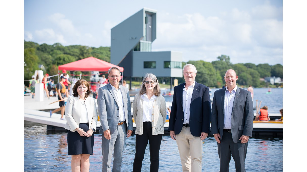 Five people stand beside Lake Banook with the tower in the background.