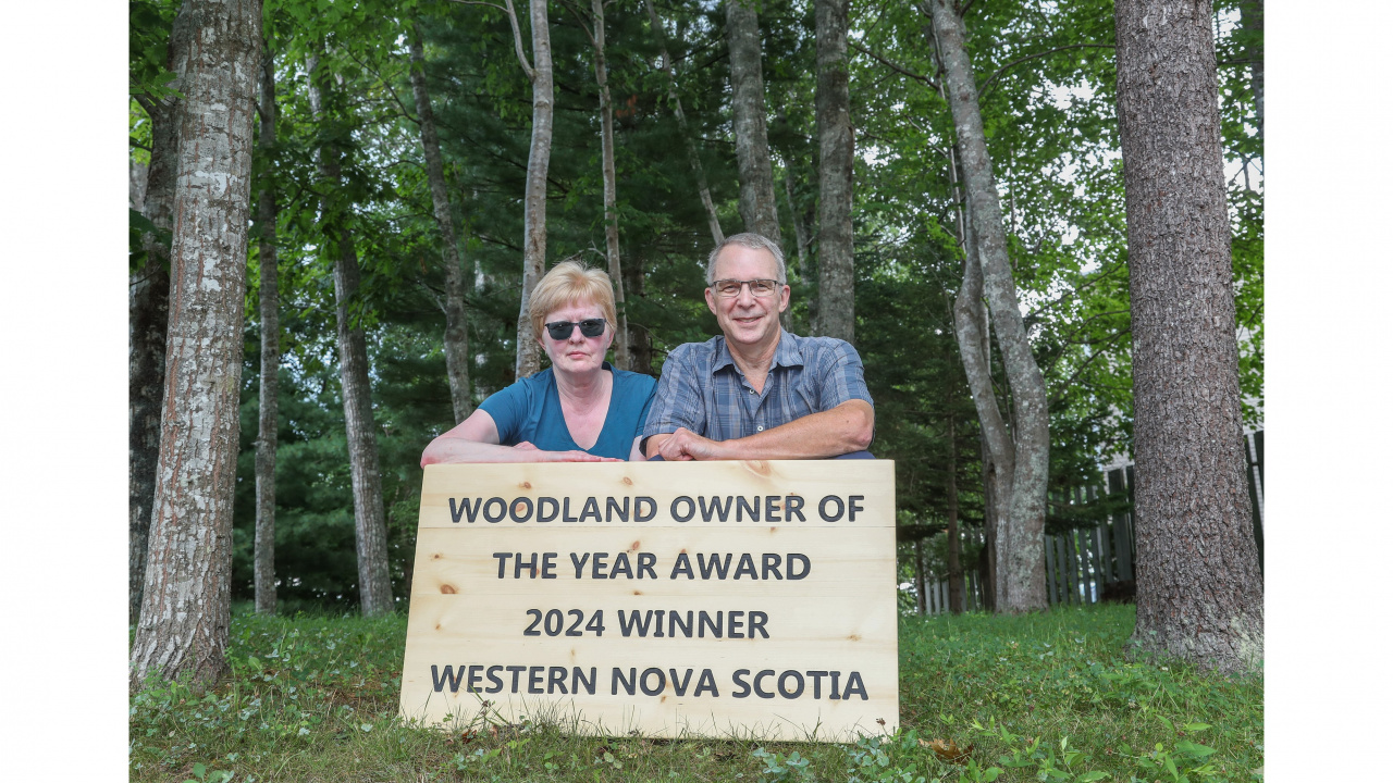 Photo of a woman and man in the woods with a sign that says Woodland Owner of the Year Award 2024 Winner Western Nova Scotia