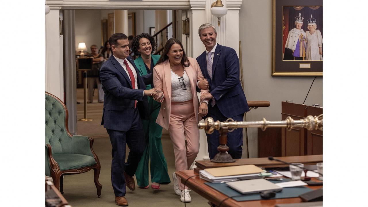 Photo of Premier Tim Houston, Official Opposition Leader Zach Churchill and NDP Leader Claudia Chender escorting new House Speaker Danielle Barkhouse in the legislative chamber