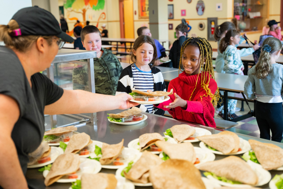 Photo of school lunch worker serving a pita to a student