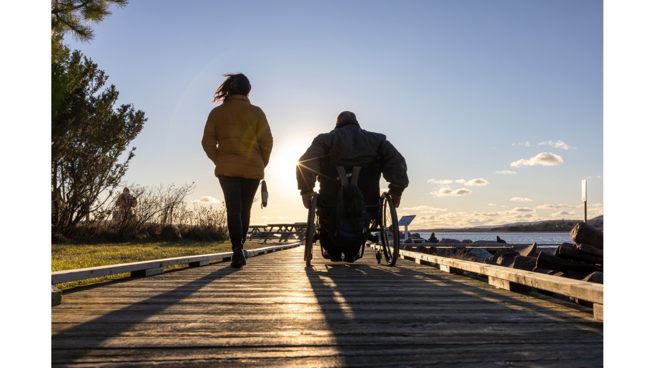 Person walking on a trail beside a person using a wheelchair, at sunrise.