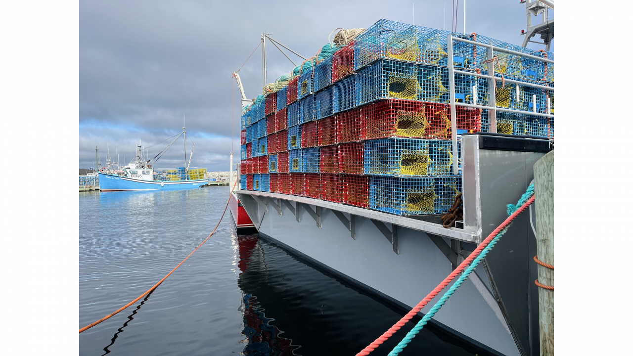 A docked boat holding many lobster traps, with a second boat and traps in the background