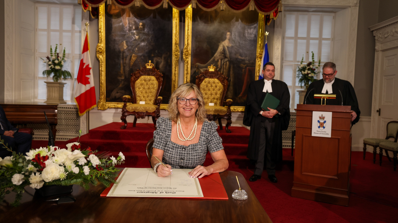 Photo of MLA Barbara Adams signing the Oath of Allegiance in the Red Chamber at Province House.