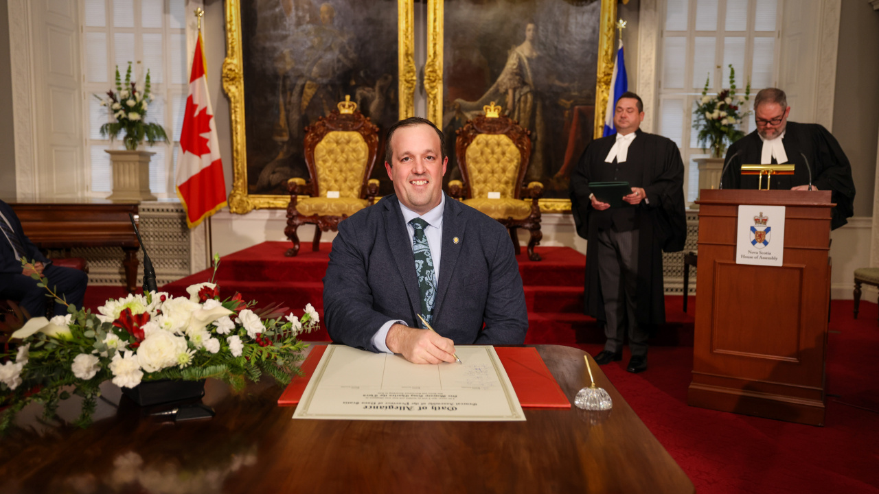 Photo of MLA Brian Comer signing the Oath of Allegiance in the Red Chamber at Province House.