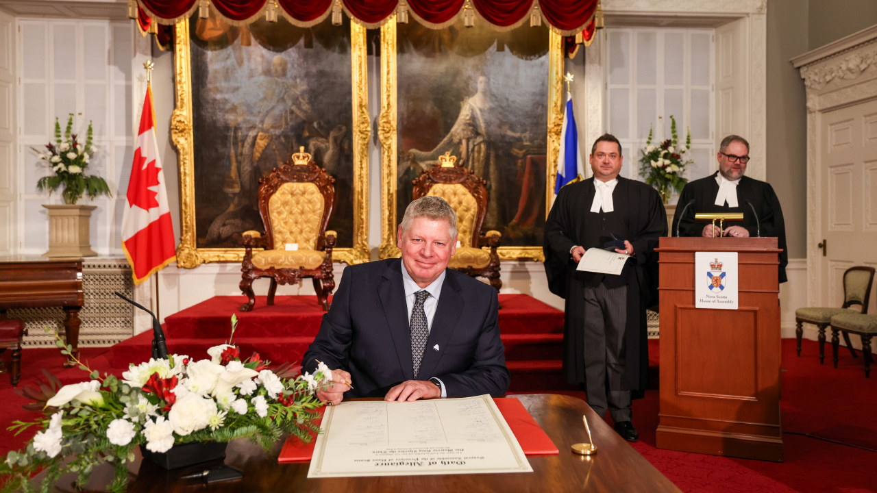 Photo of MLA David Bowlby signing the Oath of Allegiance in the Red Chamber at Province House.