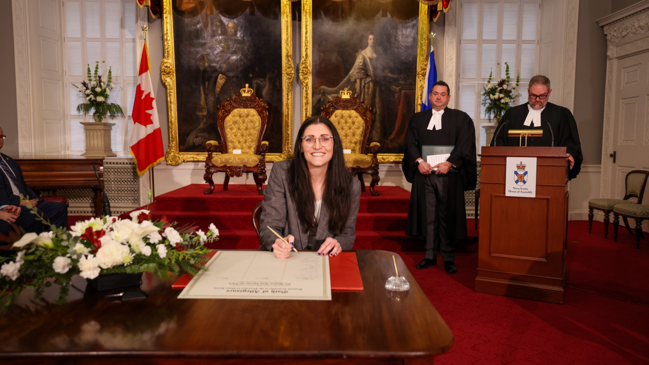 Photo of MLA Jill Balser signing the Oath of Allegiance in the Red Chamber at Province House.