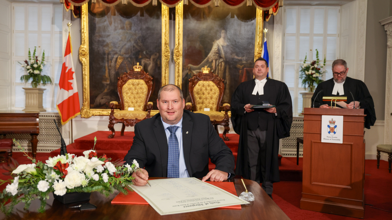 Photo of MLA Nick Hilton signing the Oath of Allegiance in the Red Chamber at Province House.