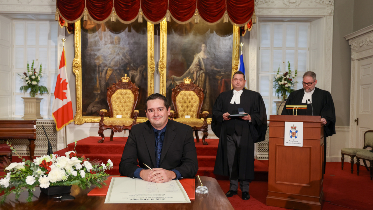 Photo of MLA Rick Burns signing the Oath of Allegiance in the Red Chamber at Province House.