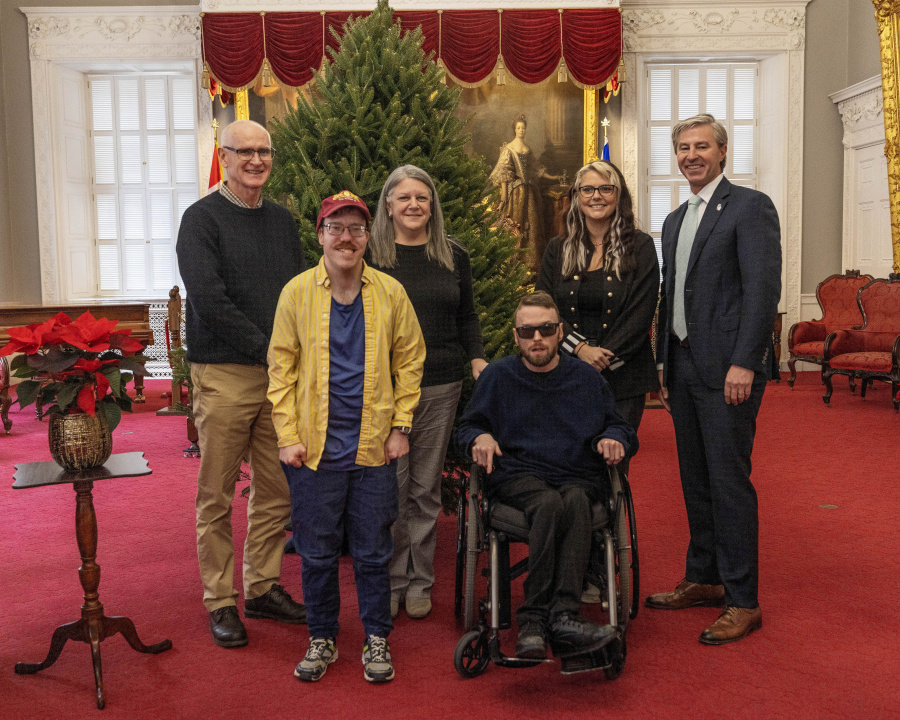 Photo of Premier Tim Houston and people from Summer Street Industries in front of an undecorated Christmas tree in the Red Chamber
