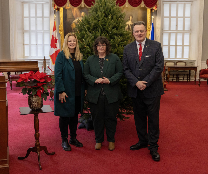 Photo of Lt.-Gov. Mike Savage with two representatives of Souls Harbour Rescue Mission in front of an undecorated Christmas tree in the Red Chamber at Province House