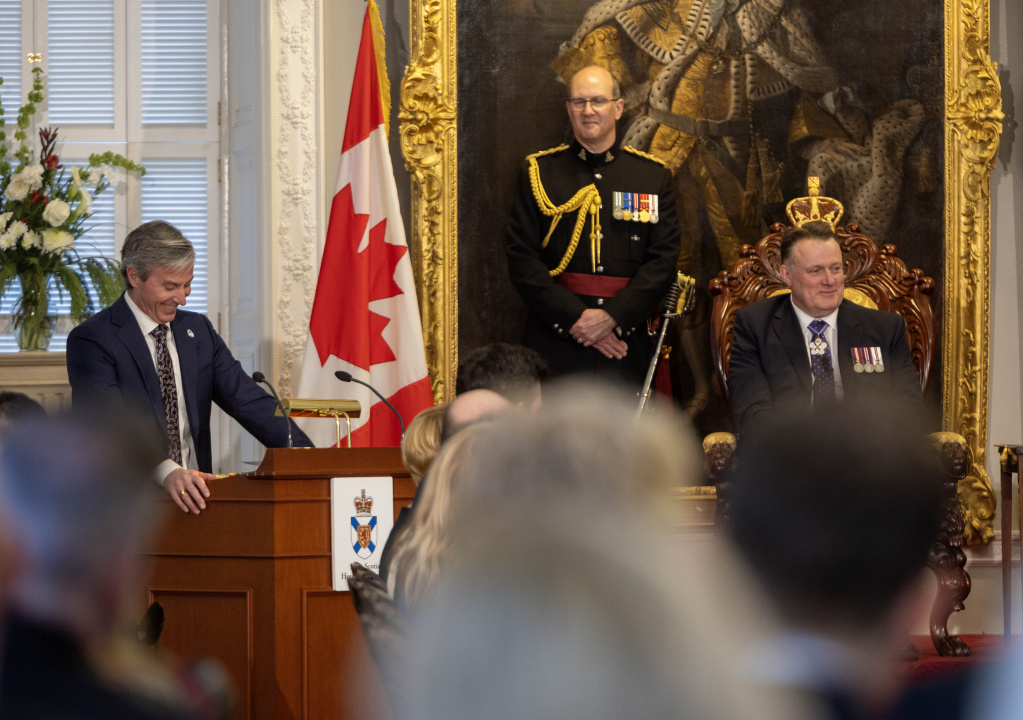 Photo of Premier Tim Houston at a podium and Lt.-Gov. Mike Savage in a chair in the Red Chamber