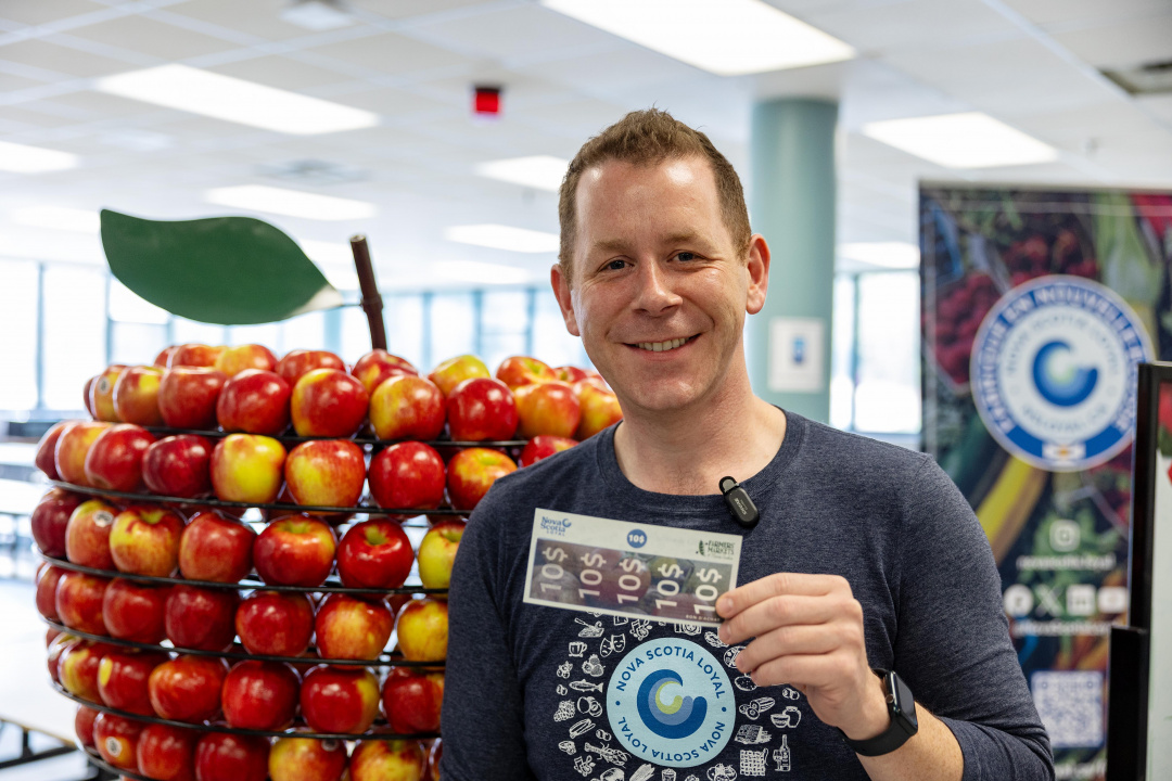 Growth and Development Minister Colton LeBlanc holds up an NS Loyal farmers' market voucher
