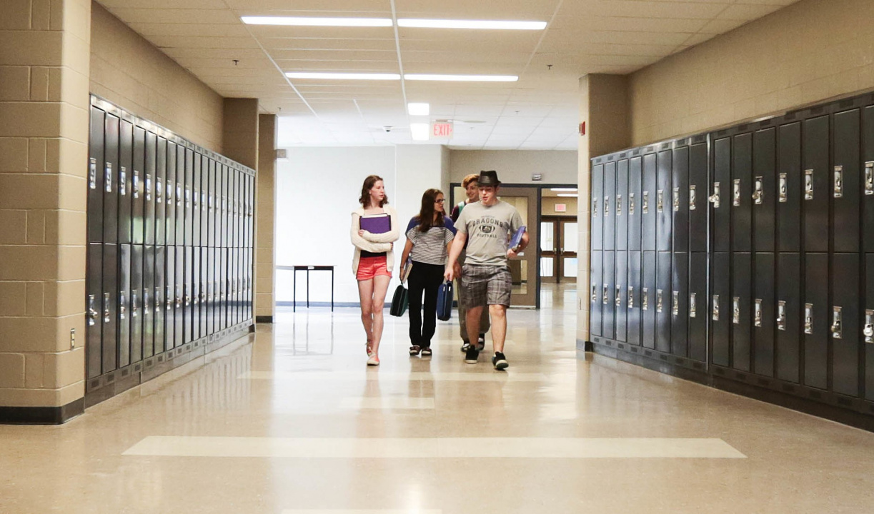Quatre élèves du secondaire marchent à côté d’un rang de casiers dans le couloir d'une école.
