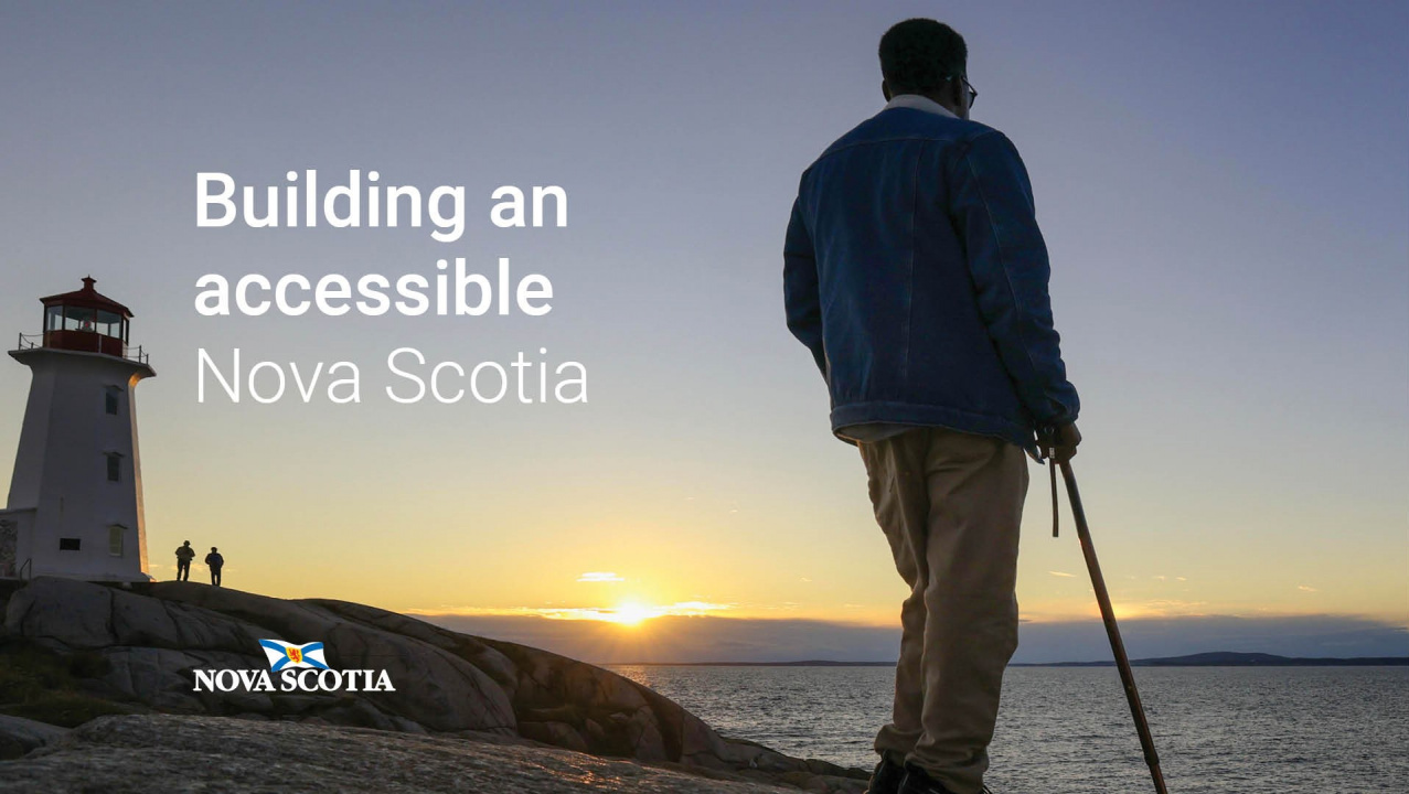 A person with a cane standing on rocks near a lighthouse at sunset