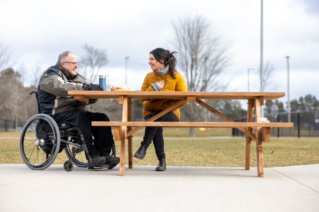 A man in a wheelchair talking with a woman at a picnic table