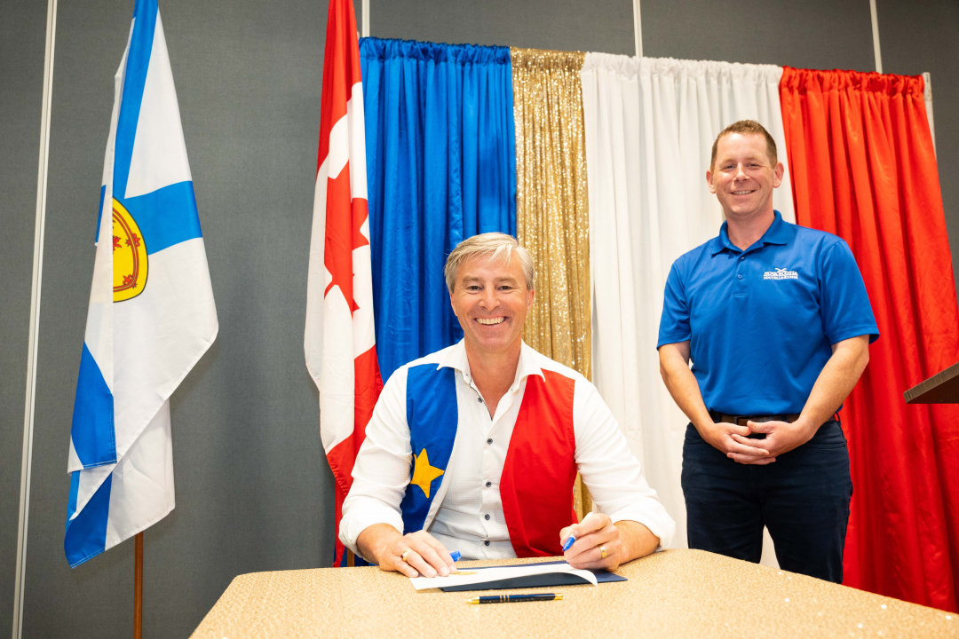 Premier Tim Houston at a table and Growth and Development Minister Colton LeBlanc standing
