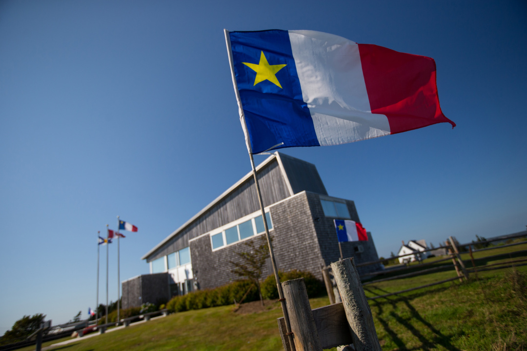The Acadian flag, with the welcome centre at the historic Acadian village in the background.
